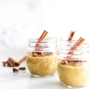 Small mason jars filled with Pumpkin Spice Chia Pudding with cinnamon sticks coming out the top of the jars