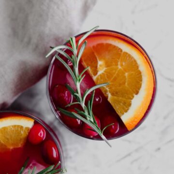 A top view of a glass filled with cranberry orange sangria, fresh cranberries, an orange slice, and a rosemary sprig on top.