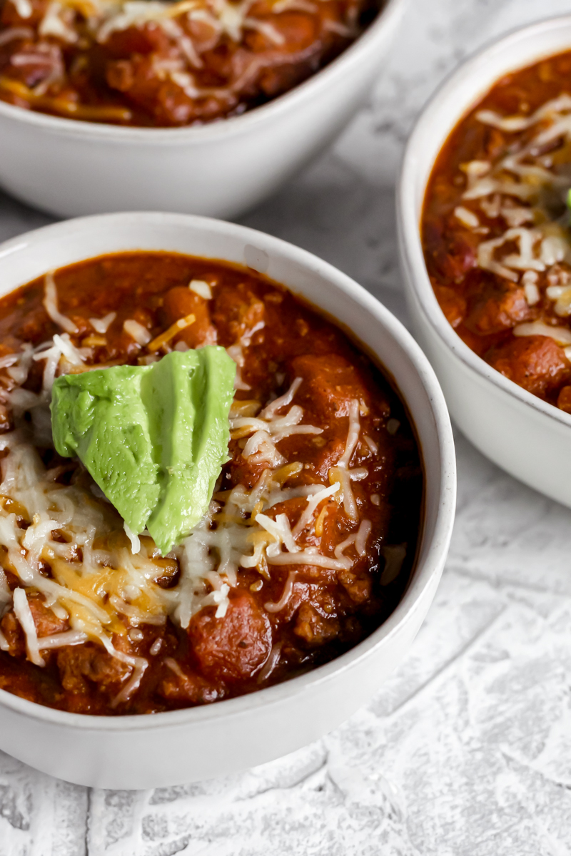 Three bowls of Southwestern Bison Chili topped with shredded cheddar cheese and avocado.