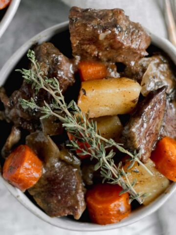 A bowl filled with Whole30 pot roast and topped with two sprigs of fresh thyme.