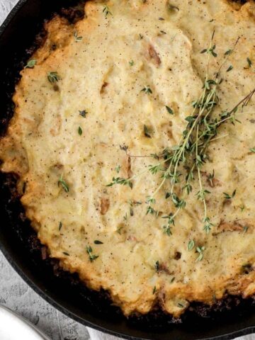 A cast iron skillet filled with bison shepherd's pie and fresh springs of thyme on top.