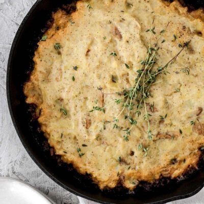 A cast iron skillet filled with bison shepherd's pie and fresh springs of thyme on top.