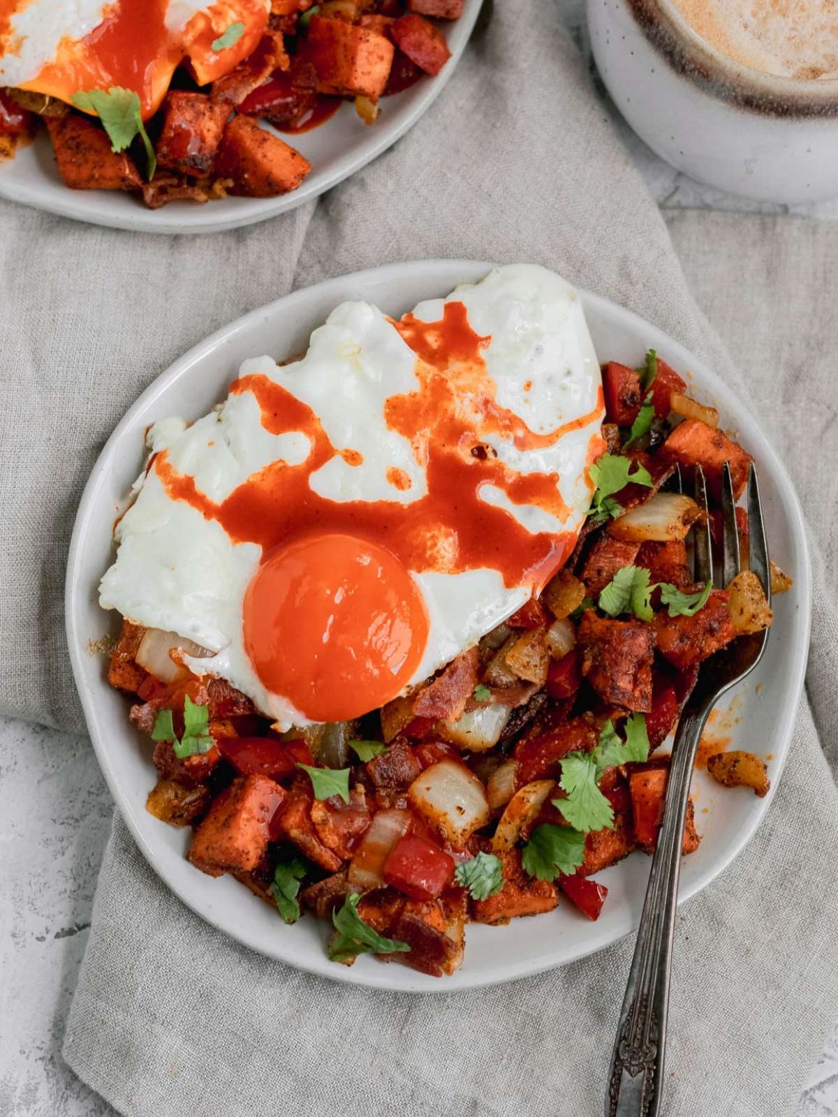A plate with whole30 sweet potato hash topped with an egg and hot sauce drizzled on top