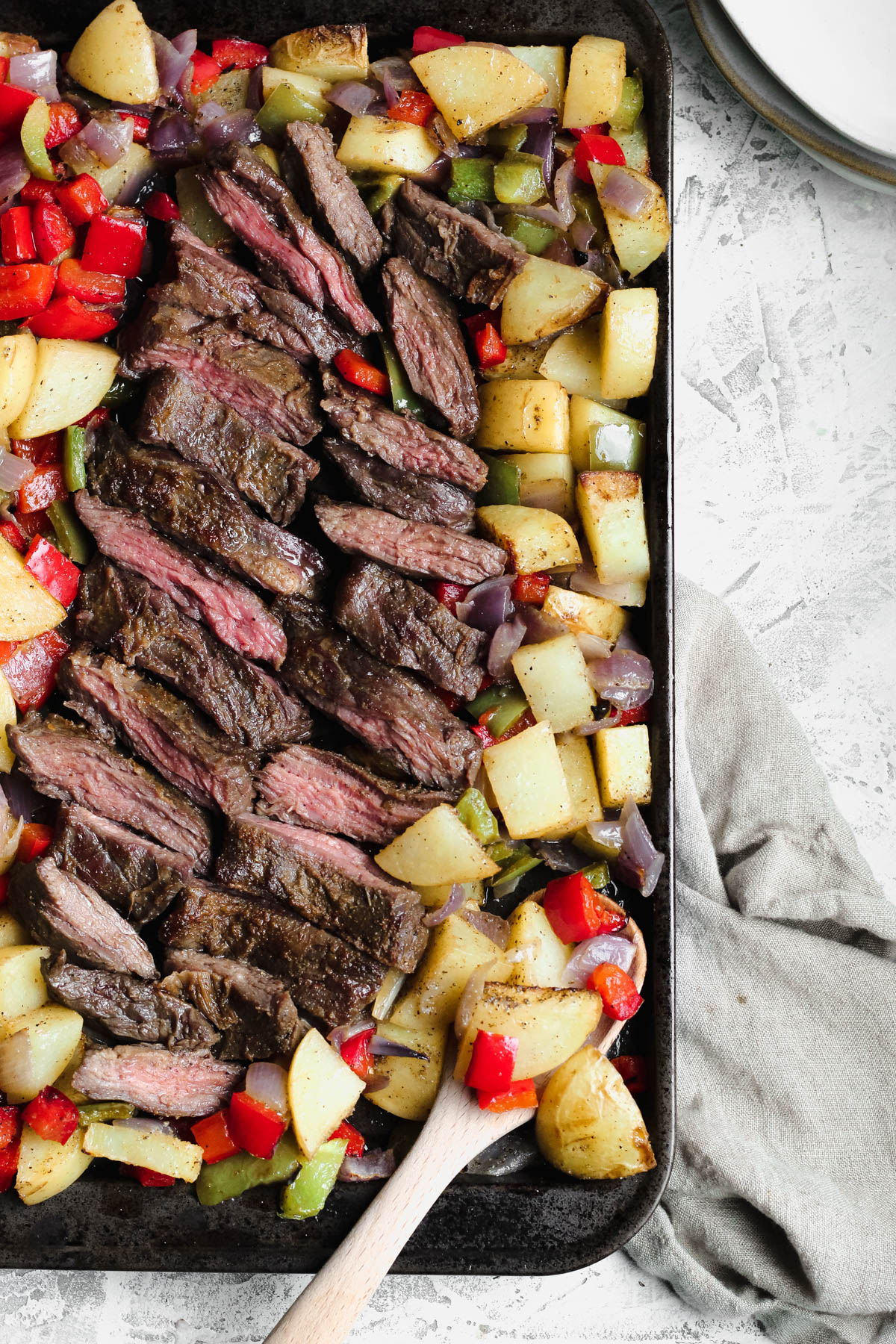 a cooking sheet filled with cooked skirt steak and roasted potatoes and onions