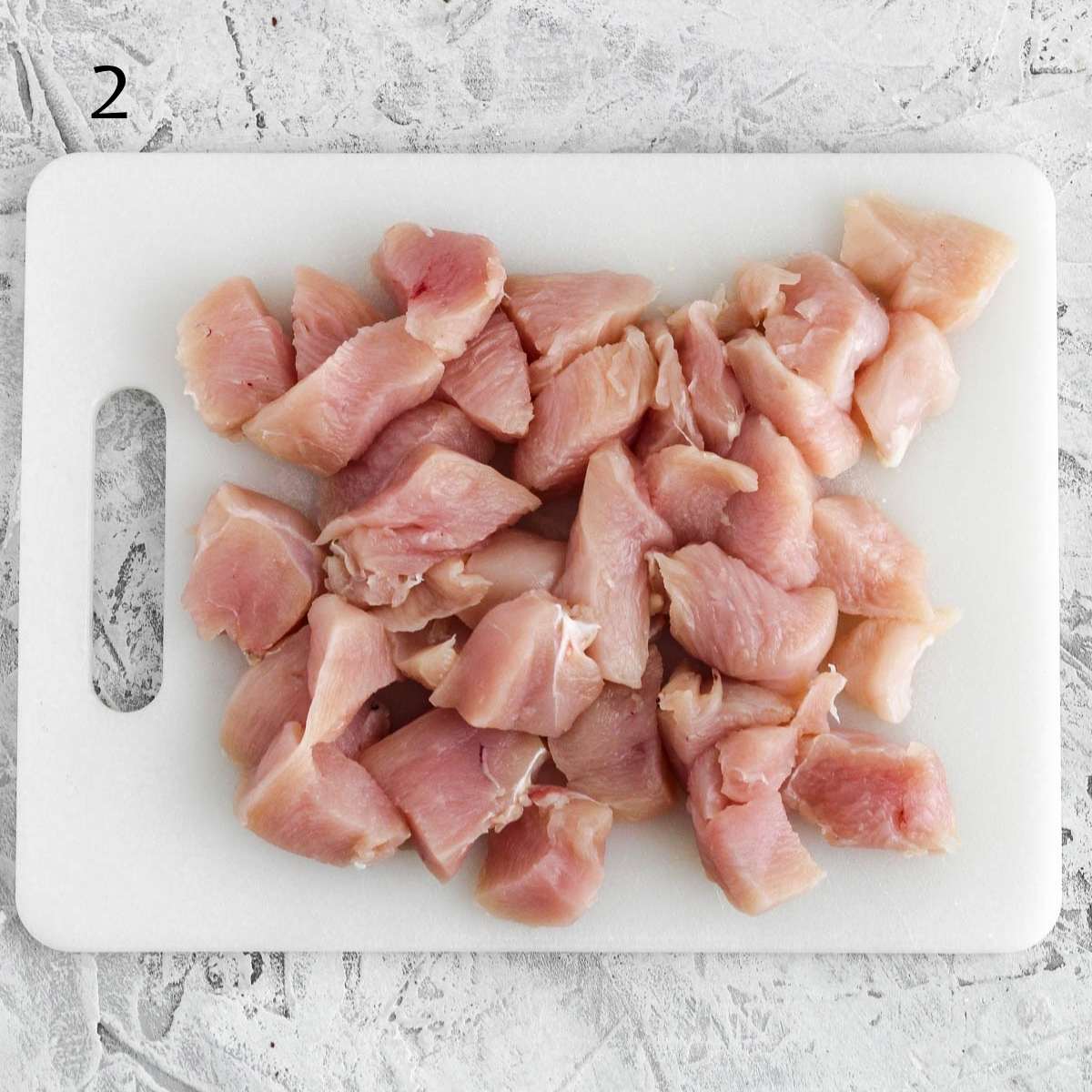 a cutting board with chicken cut into cubes