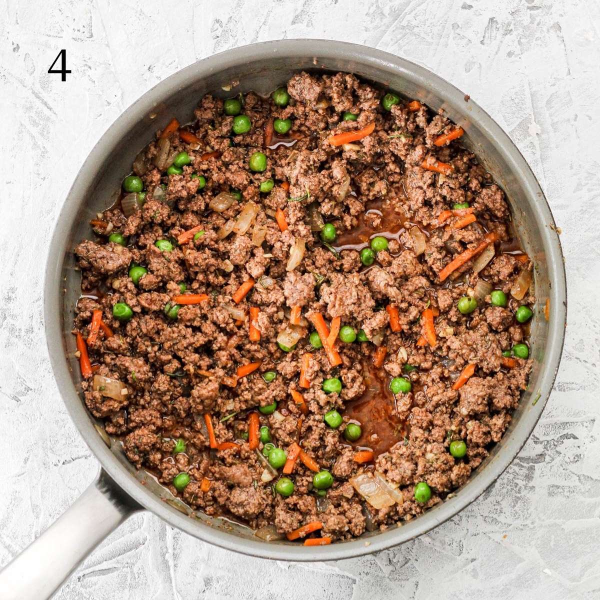 A pan with ground bison, frozen peas and carrots, and coconut aminos.
