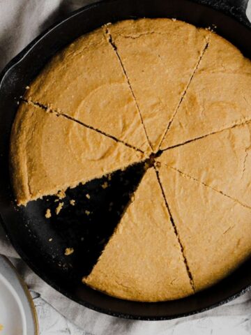 Gluten free cornbread in a cast iron skillet with a slice missing.