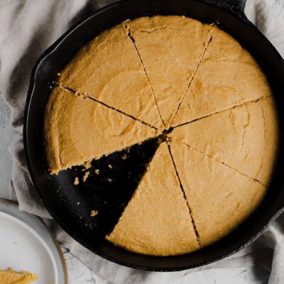 Gluten free cornbread in a cast iron skillet with a slice missing.