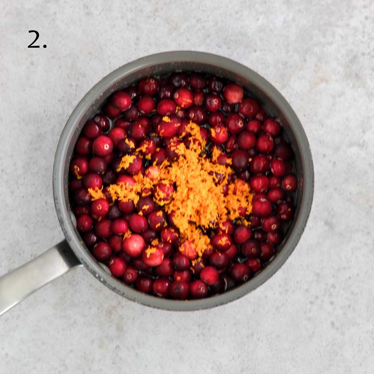 A sauce pan filled with fresh cranberries, orange juice, honey, and orange zest