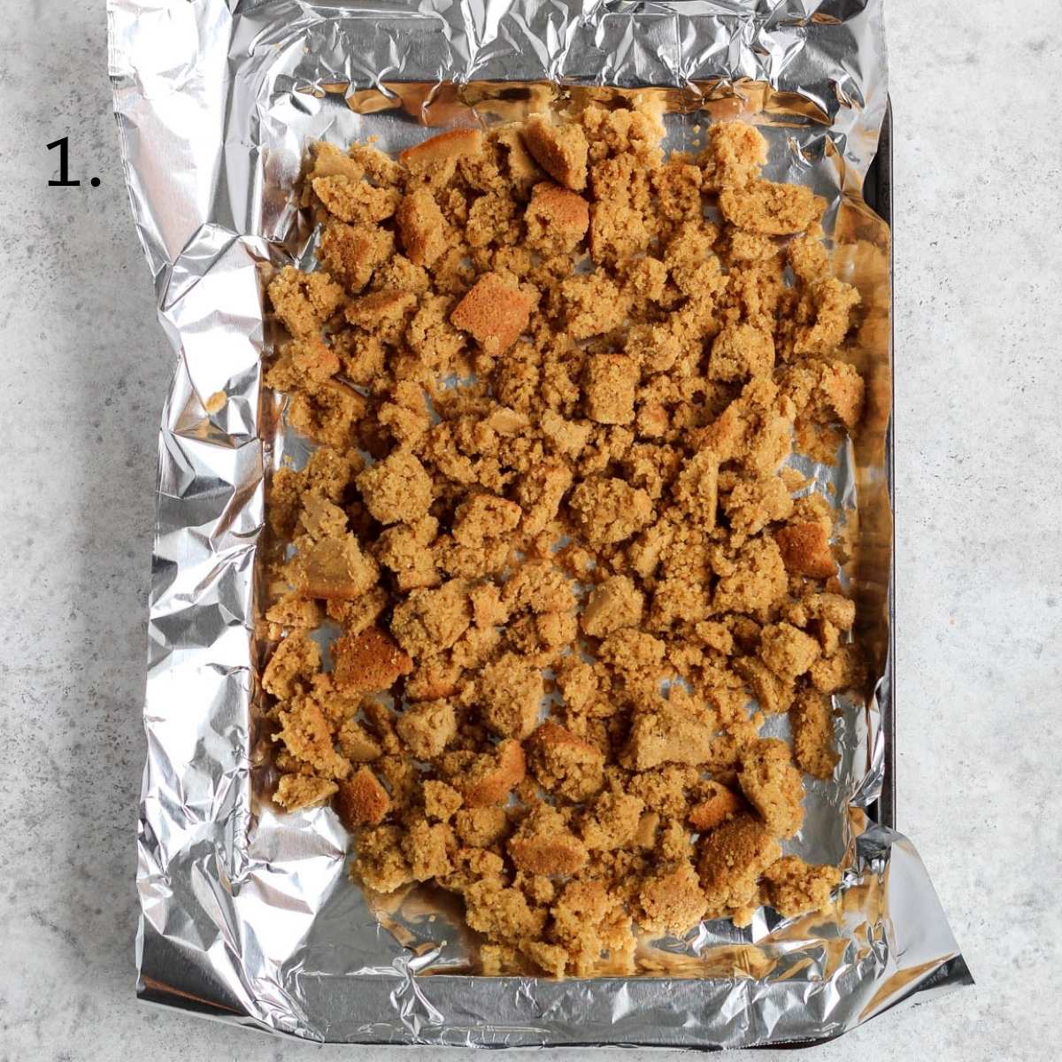 A cookie sheet lined with foil filled with gluten free cornbread crumbled on top.