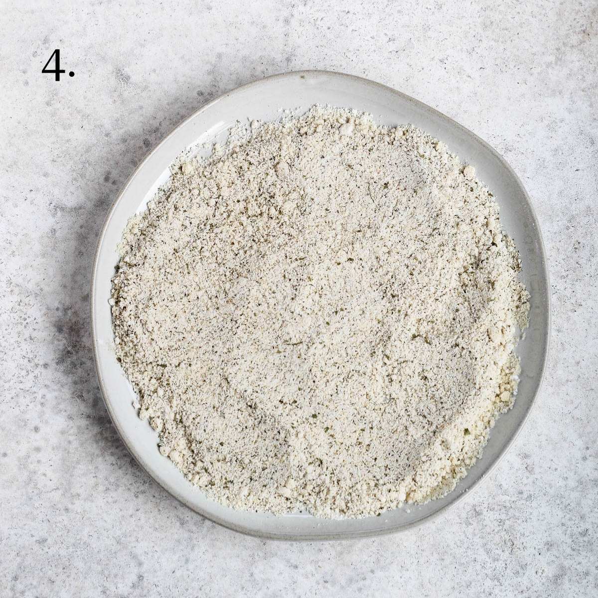 A plate with mixed almond flour, tapioca flour, garlic powder, onion powder, dried parsley, salt, and pepper.