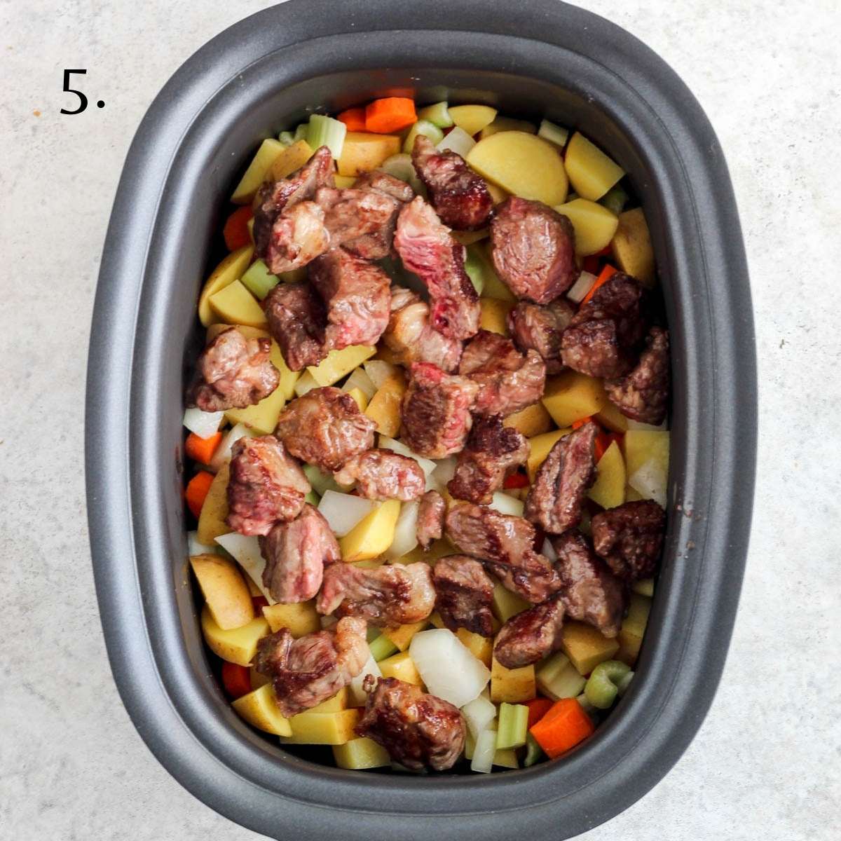 A crock pot filled with chcuk roast, potatoes, carrots, onions, and celery.