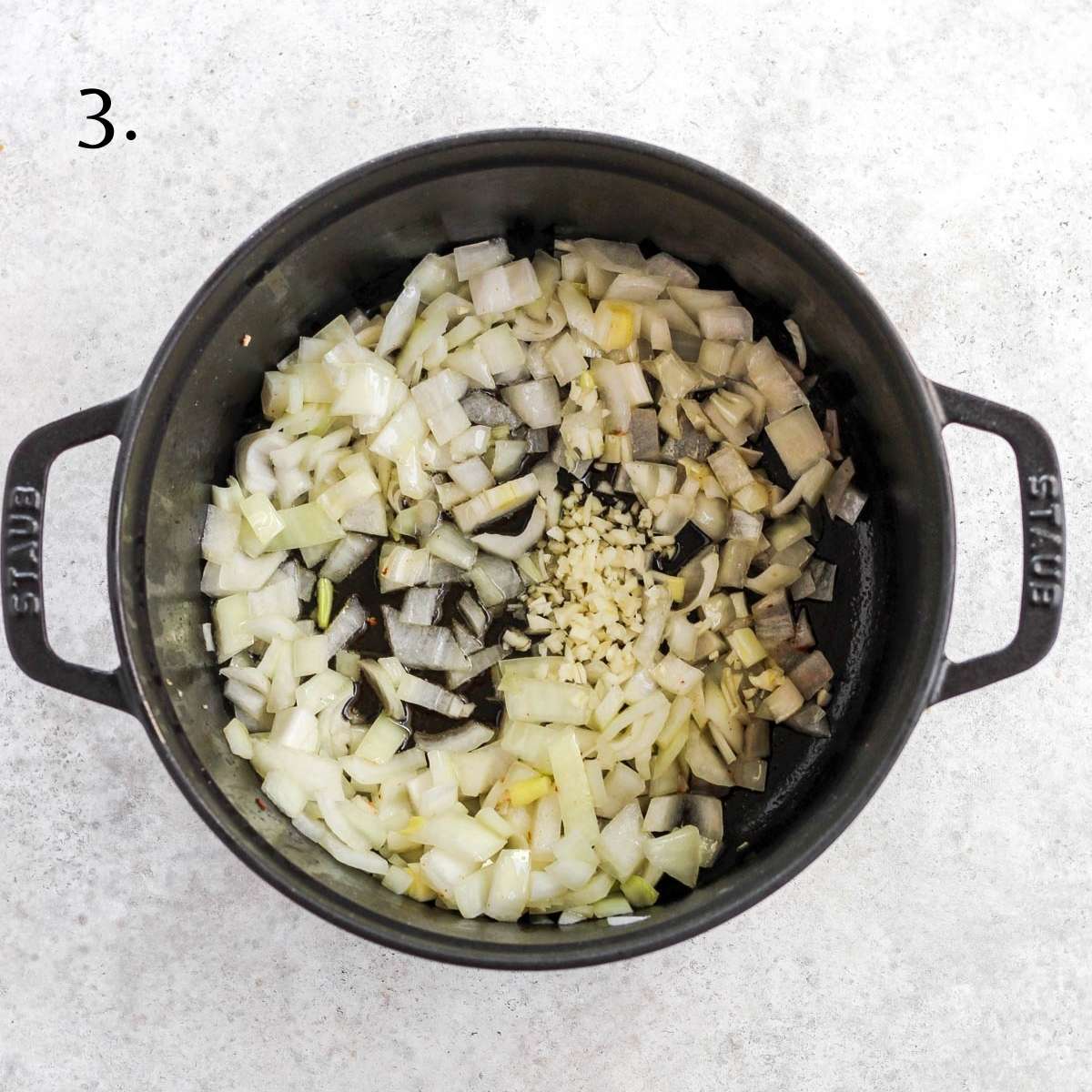 A dutch oven with diced onions, minced garlic, and ghee inside.