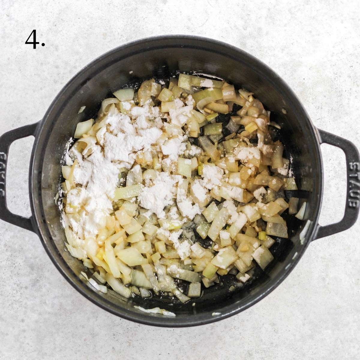 A dutch oven with sauted onions, minced garlic, and arrowroot flour sprinkled on top.
