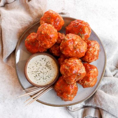 A plate filled with buffalo turkey meatballs with a side of ranch and toothpicks also sitting on the plate.