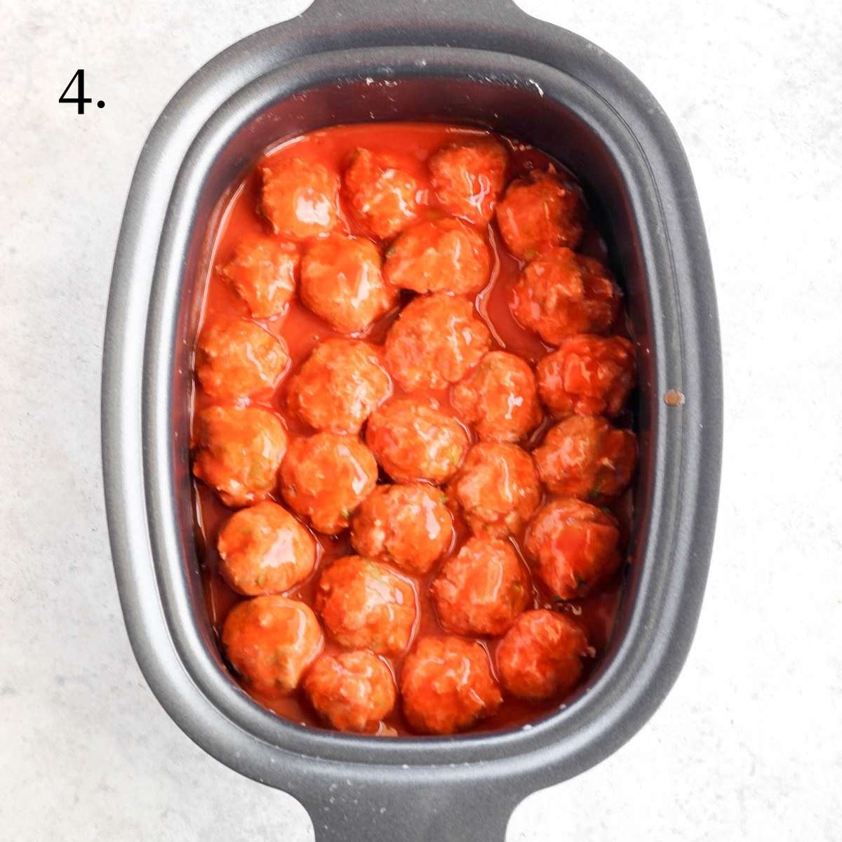 A crockpot filled with uncooked turkey meatballs covered in hot sauce.