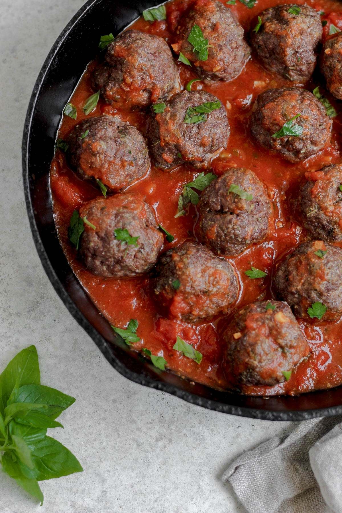 A cast iron skillet filled with sauce and bison meatballs.