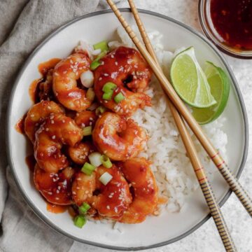 A bowl filled with white rice and topped with honey sriracha shrimp with a garnish of lime and chopsticks sitting on the side of the bowl.