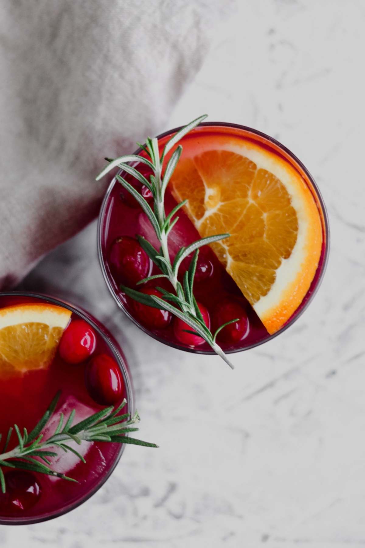 A top down view of a glass filled with cranberry orange sangria, fresh cranberries, an orange slice, and a fresh rosemary sprig.