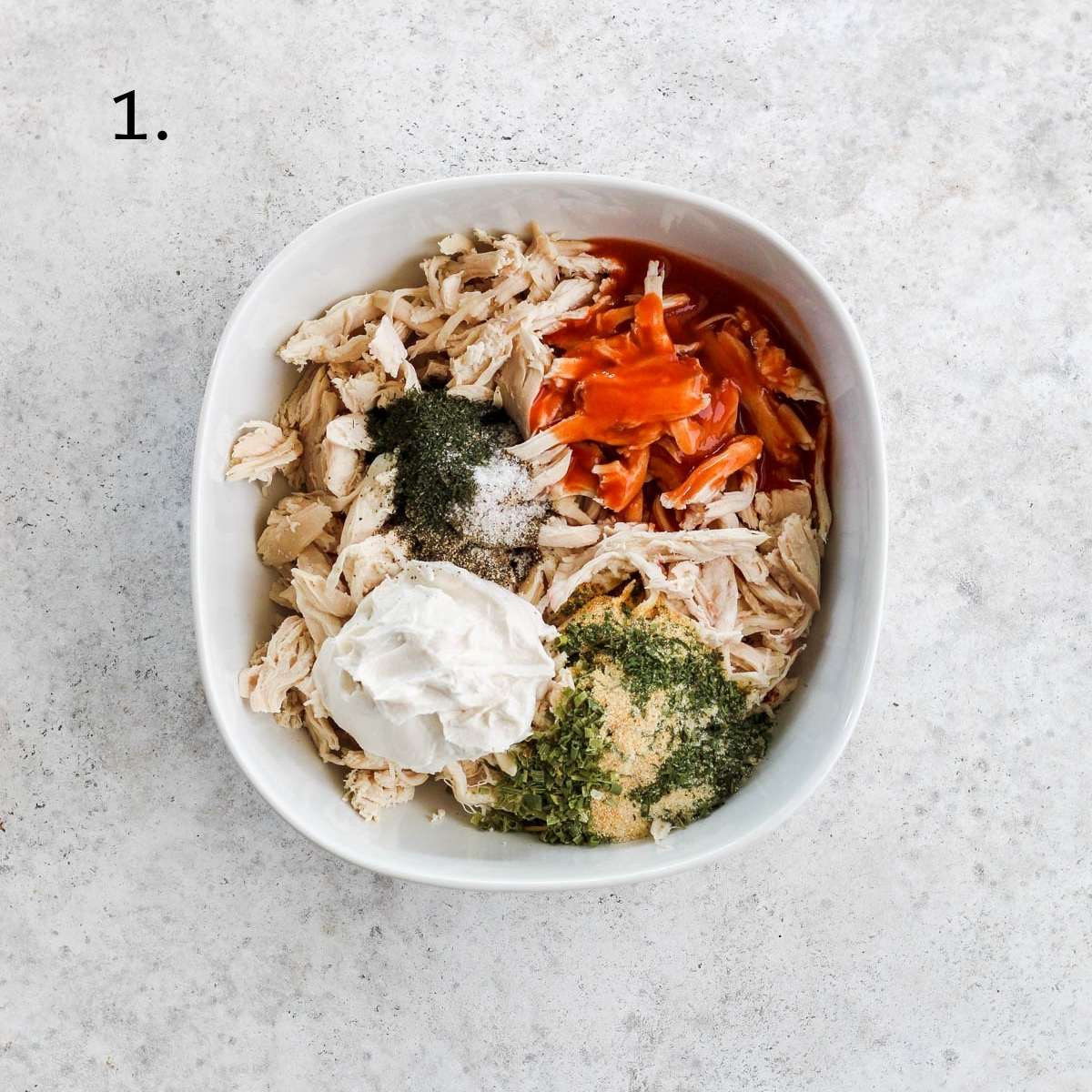 A white bowl filled with shredded chicken, dairy free cream cheese, seasonings, and hot sauce.
