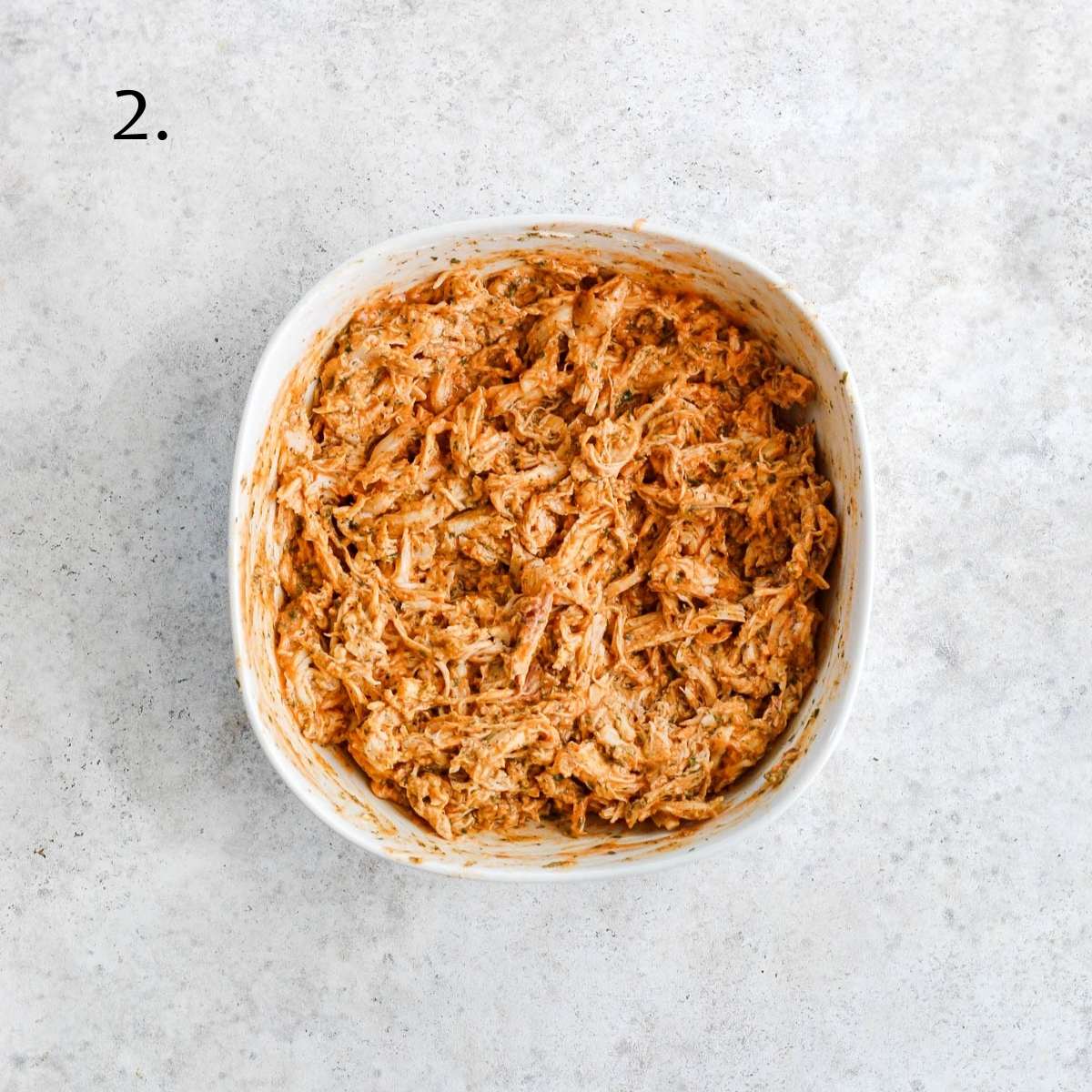 A white bowl filled with shredded chicken, dairy free cream cheese, seasonings, and hot sauce mixed together.