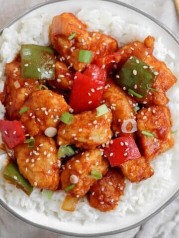 A bowl filled with white rice and topped with gluten free sweet and sour chicken that is sitting on top of a tan towel.