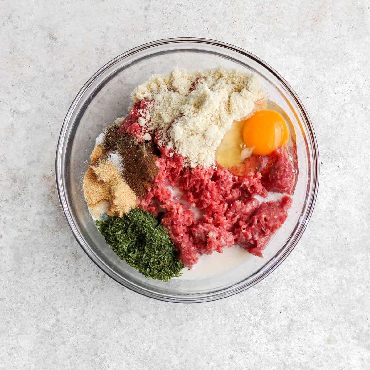 A glass bowl filled with Swedish meatball ingedients.