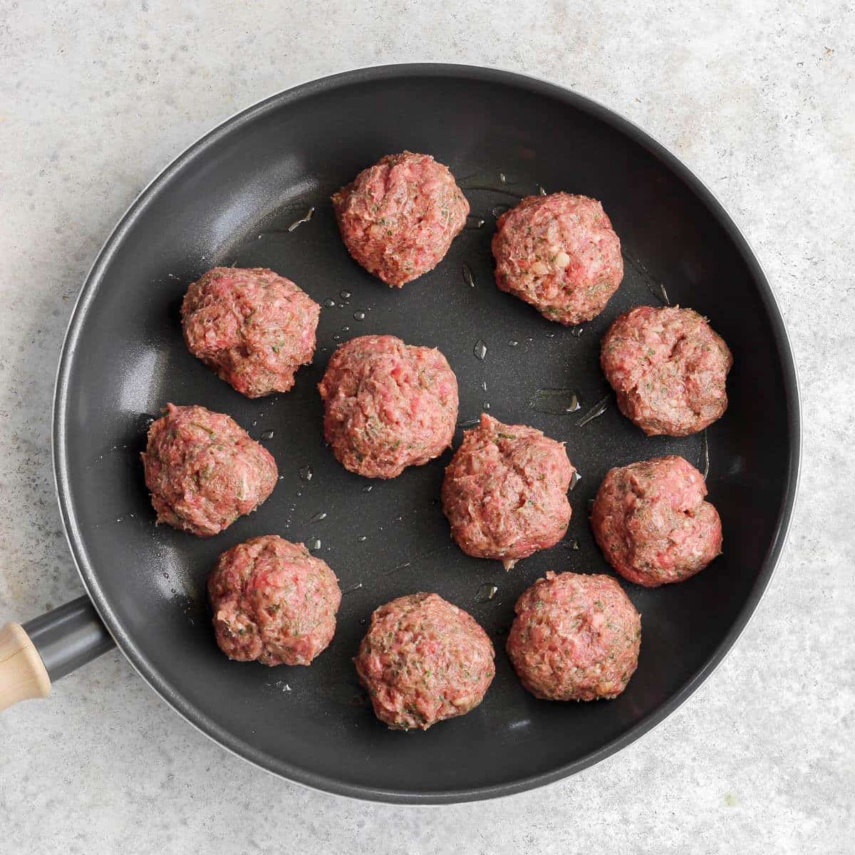 A pan filled with uncooked meatballs.