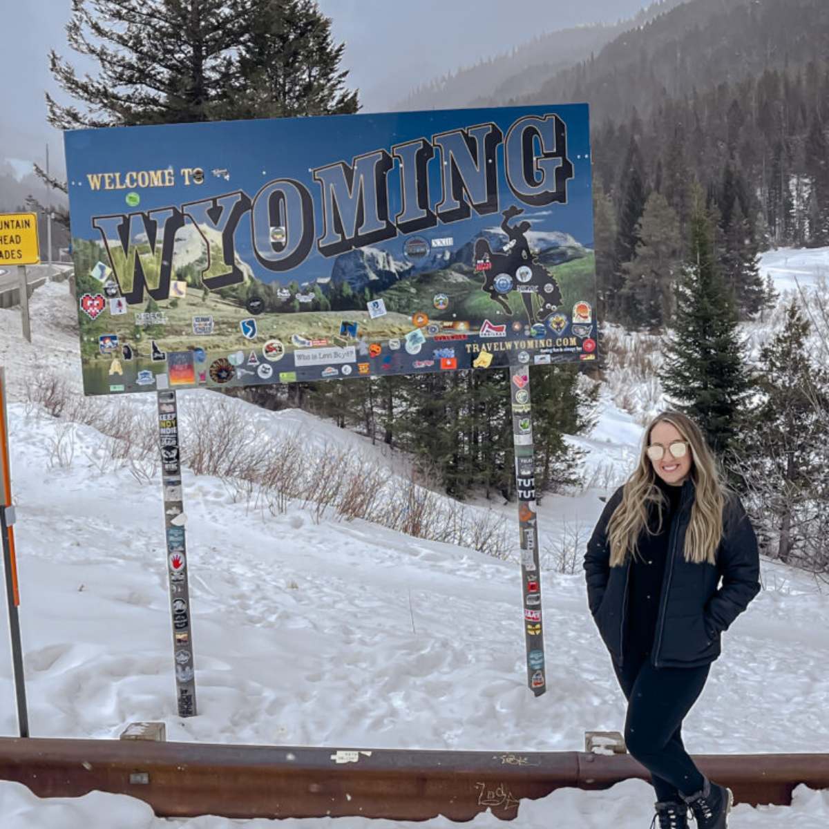 A girl standing in front of the Wyoming sign in the snow.