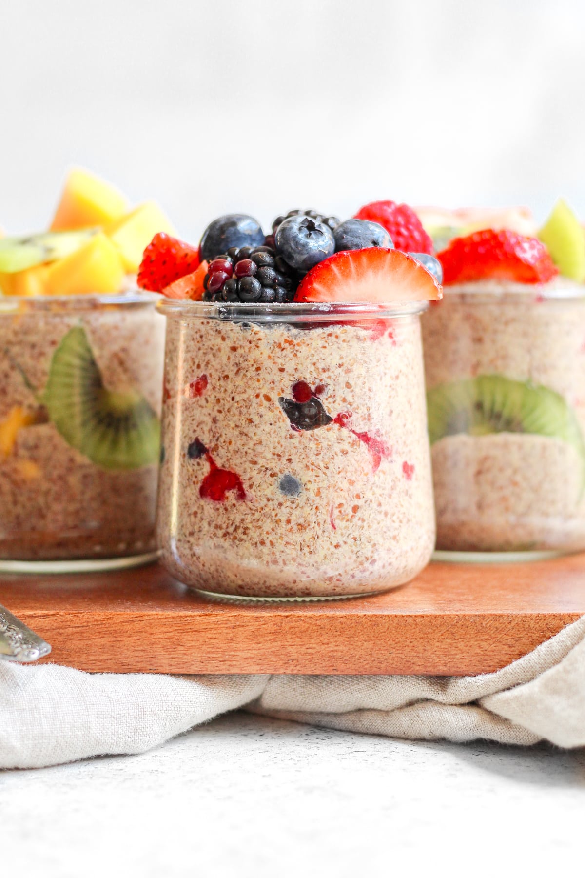 Three jars of flaxseed pudding topped with berries and sitting on a brown cutting board.