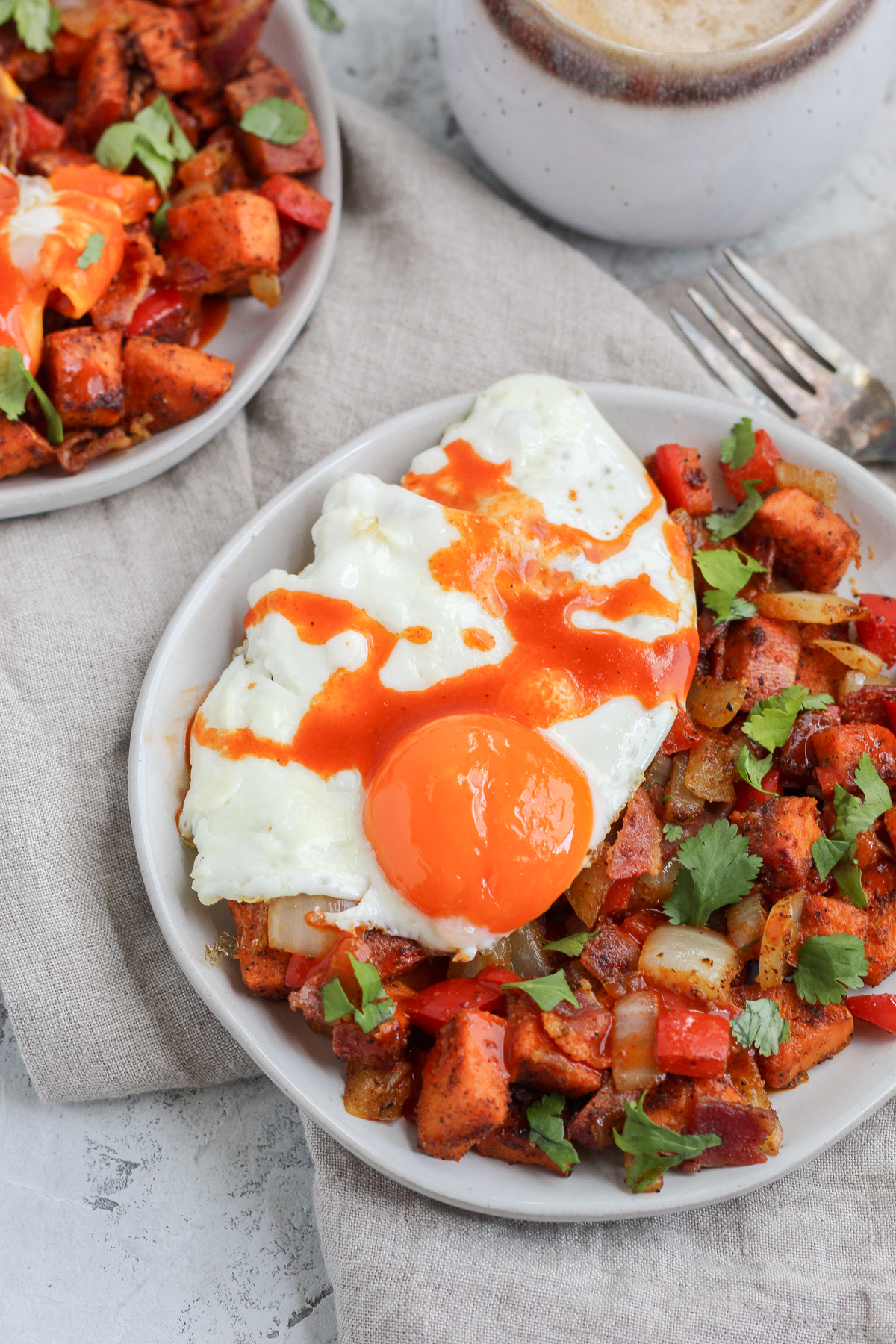 A plate filled with sweet potato hash topped with a sunny side up egg and hot sauce.