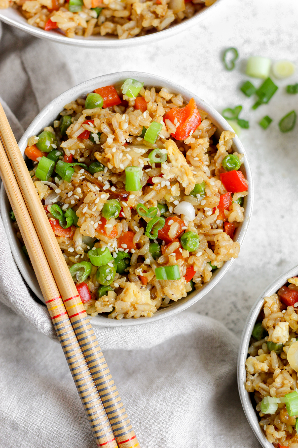 A bowl filled with gluten free fried rice sitting on a tea towel with chopsticks resting on top of the bowl.