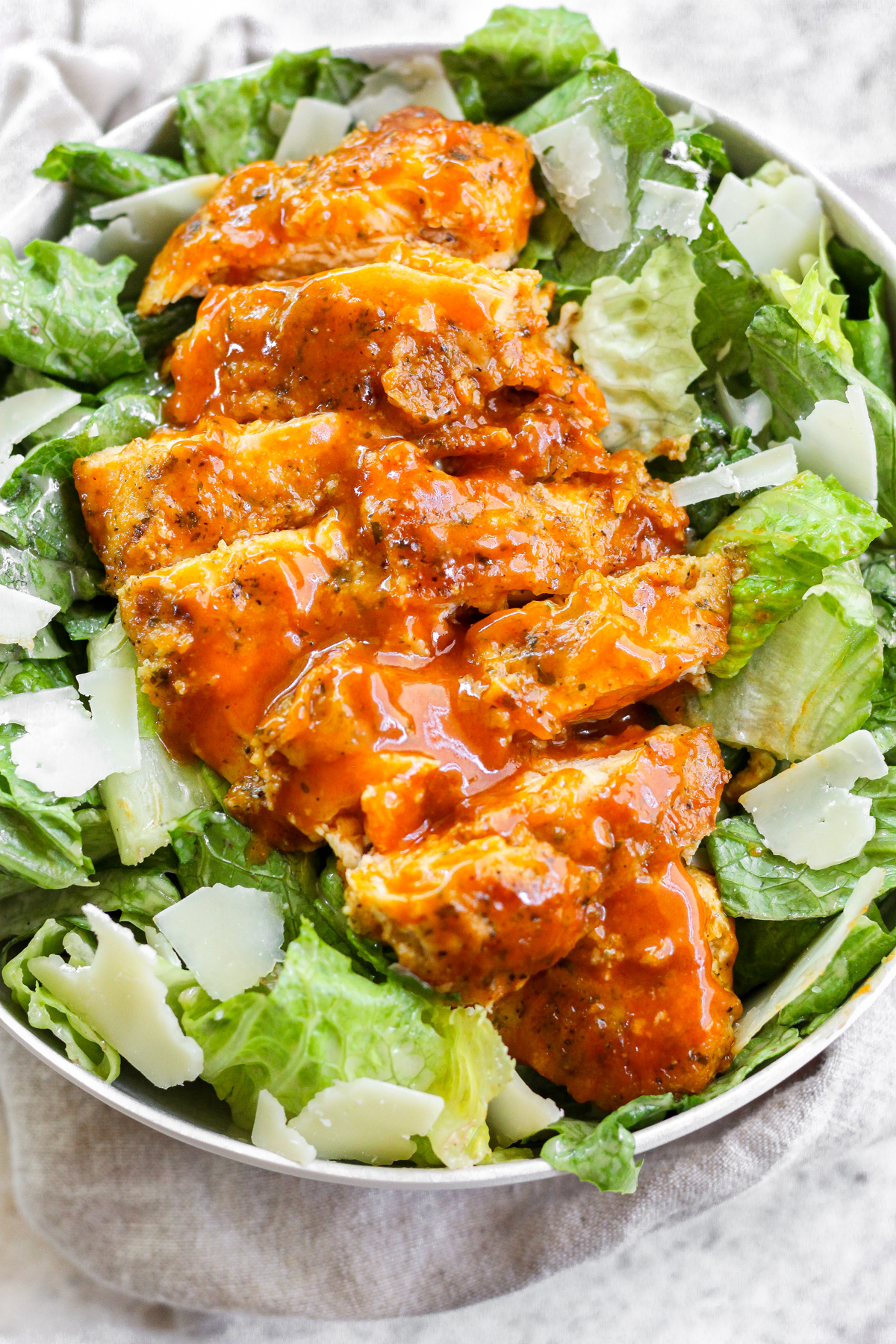 Buffalo chicken laying on top of caesar salad.