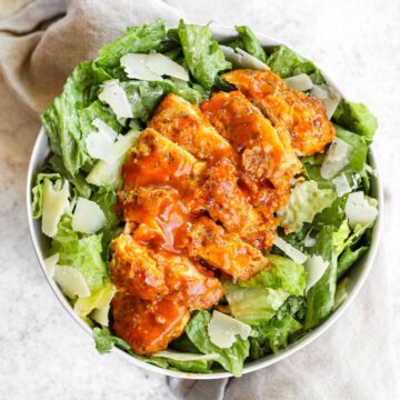 Buffalo chicken laying on top of caesar salad.