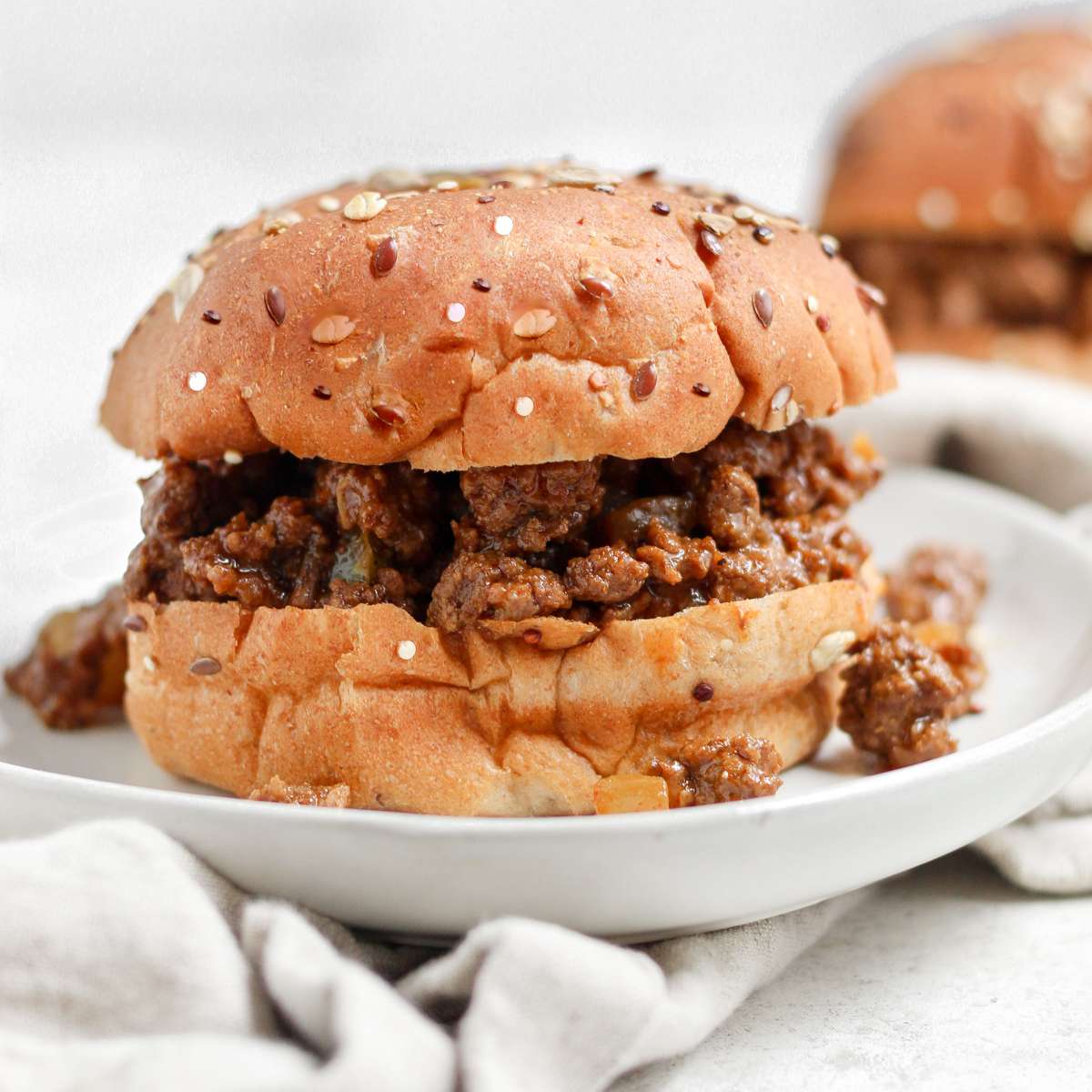 A bison sloppy joe sitting on a plate that is sitting on a tea towel.