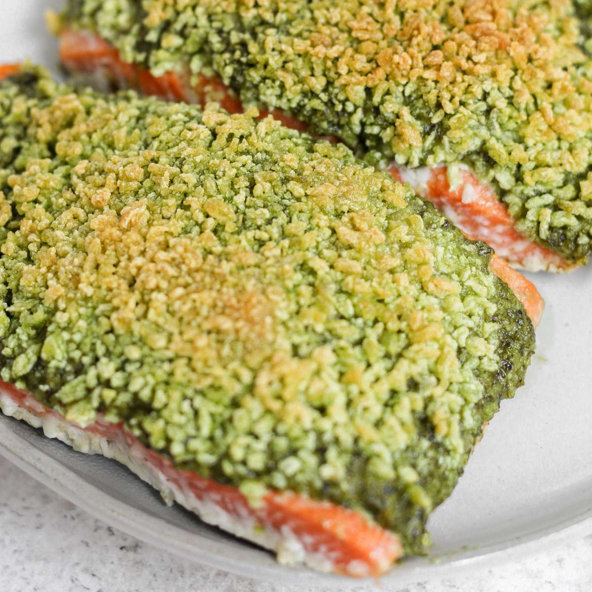 Pesto crusted salmon sitting on a plate.