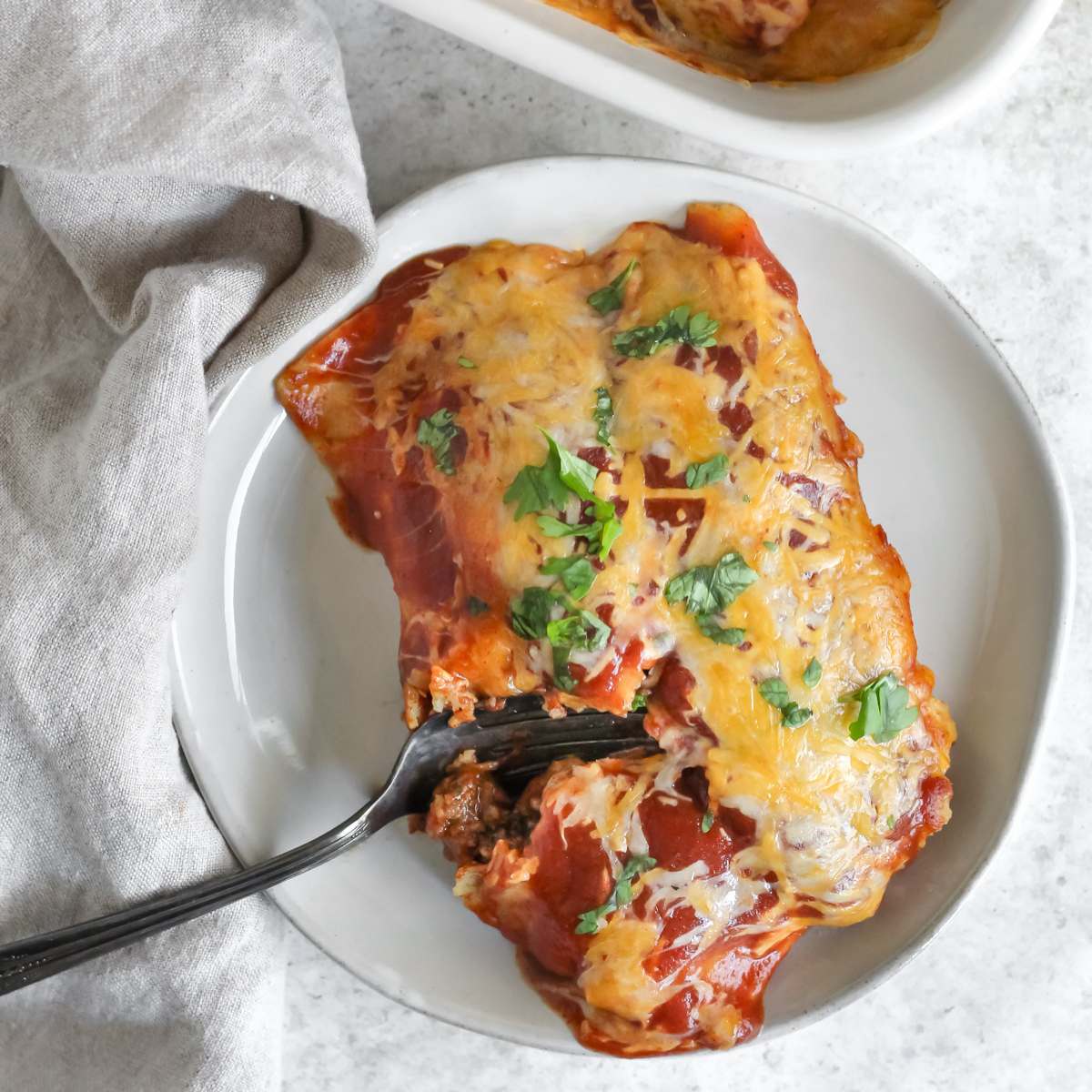 Two enchiladas on a plate with a fork breaking one of them open.