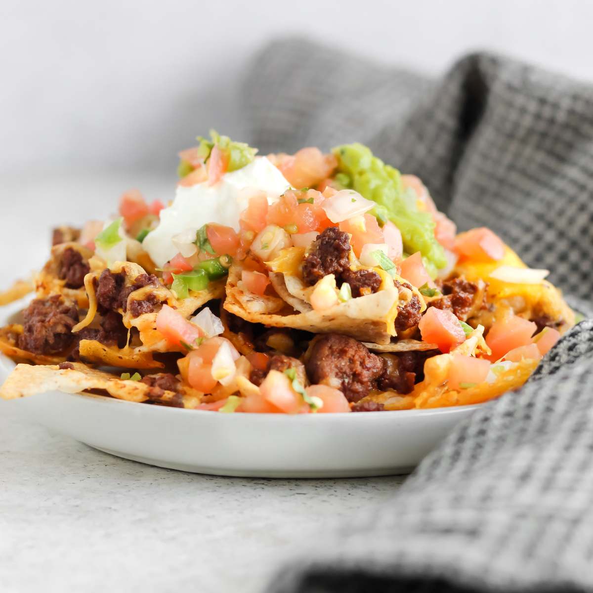 A plate filled with ground bison nachos and topped with sour cream, guacamole, and pico de gallo.