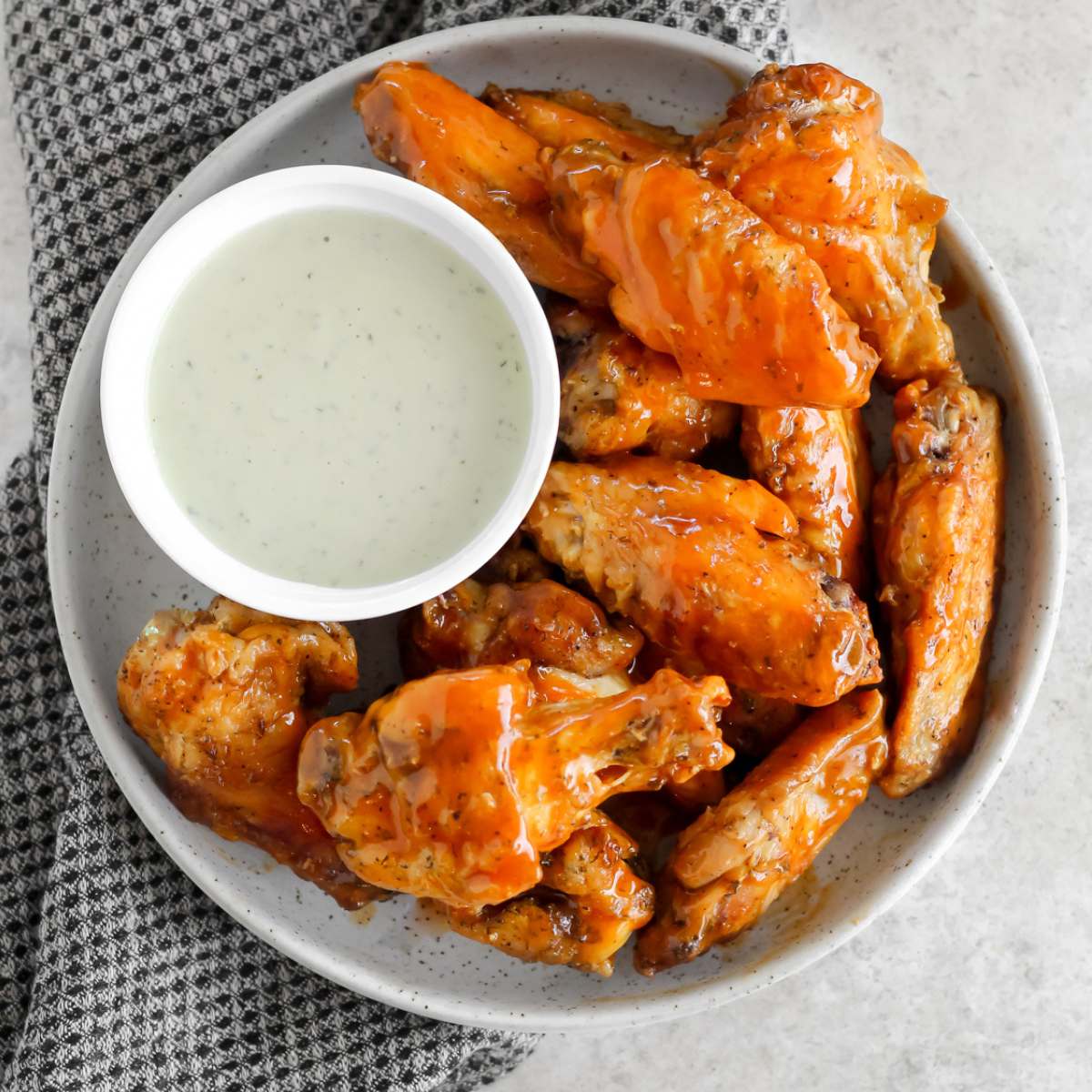 Gluten free chicken wings on a plate with a side ranch and the plate sitting on a black tea towel.