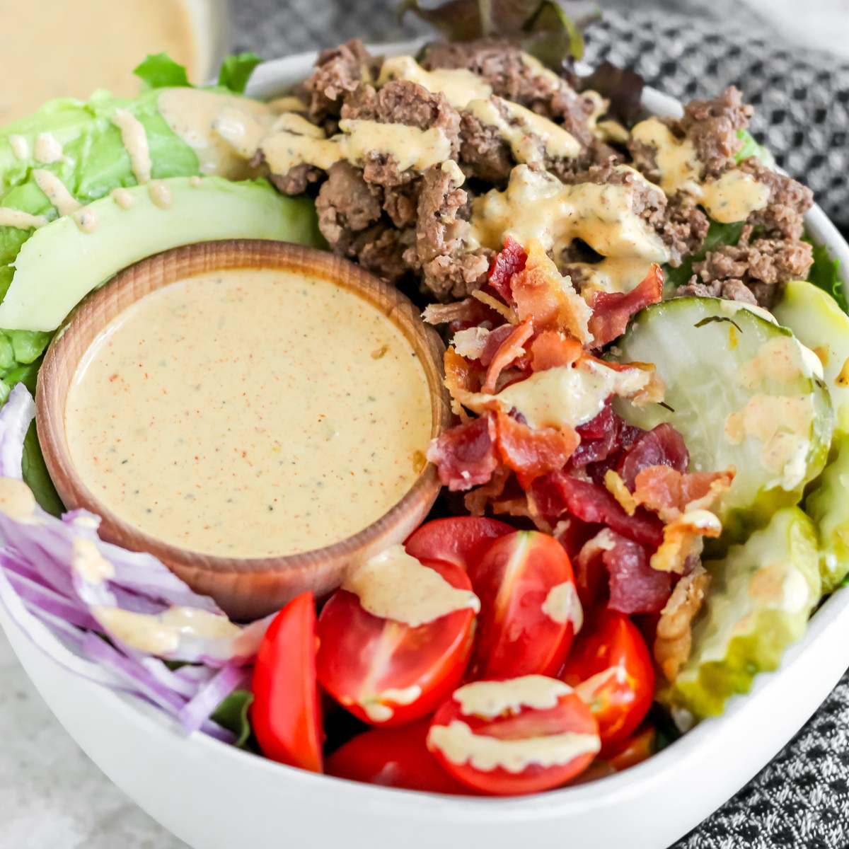A bowl filled with lettuce, tomatoes, avocado, onions, pickles, ground bison, and special sauce.