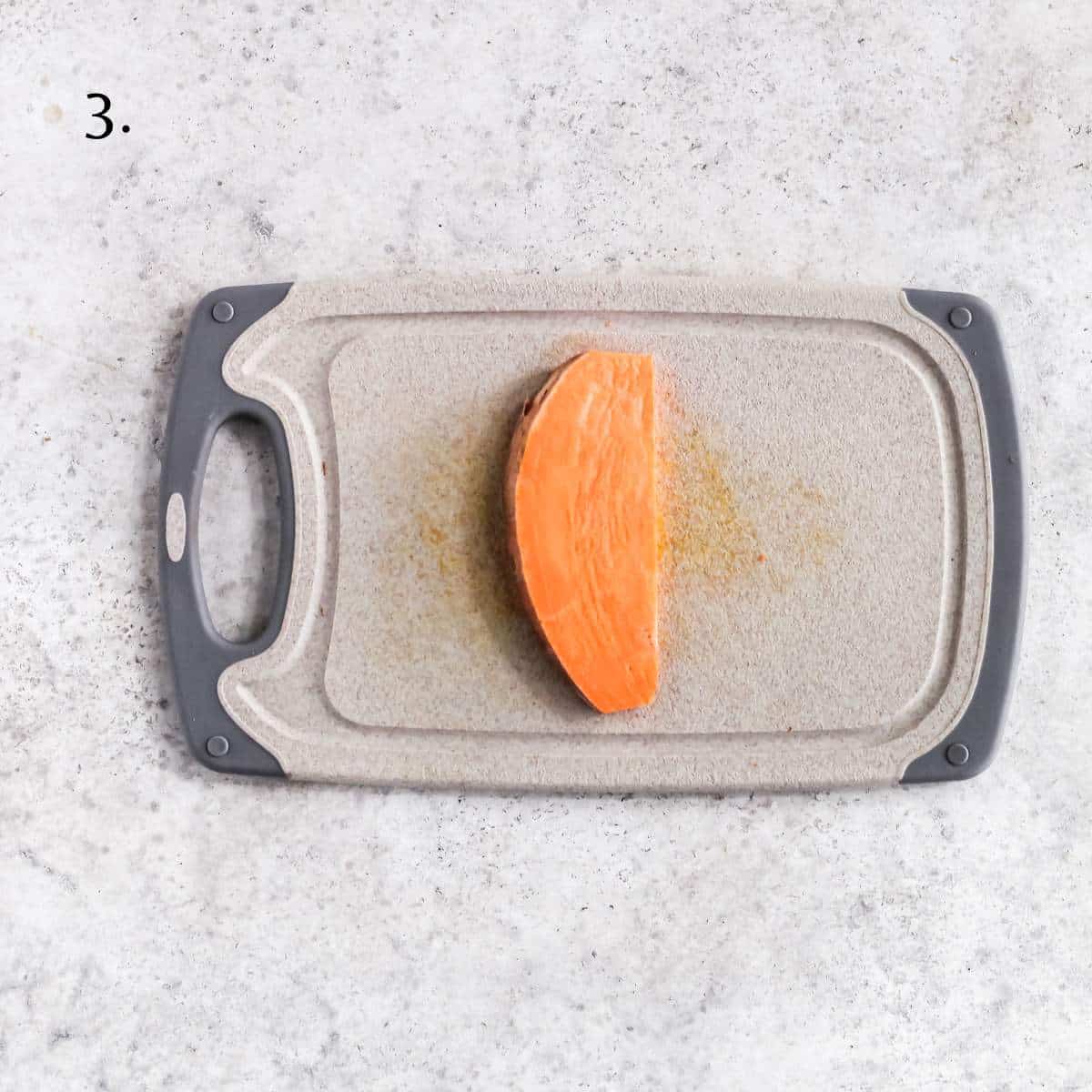 A slice of uncooked sweet potato sitting on a cutting board.