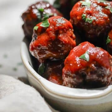 BBQ bison meatballs sprinkled with parsley on top sitting in an oval shaped dish.