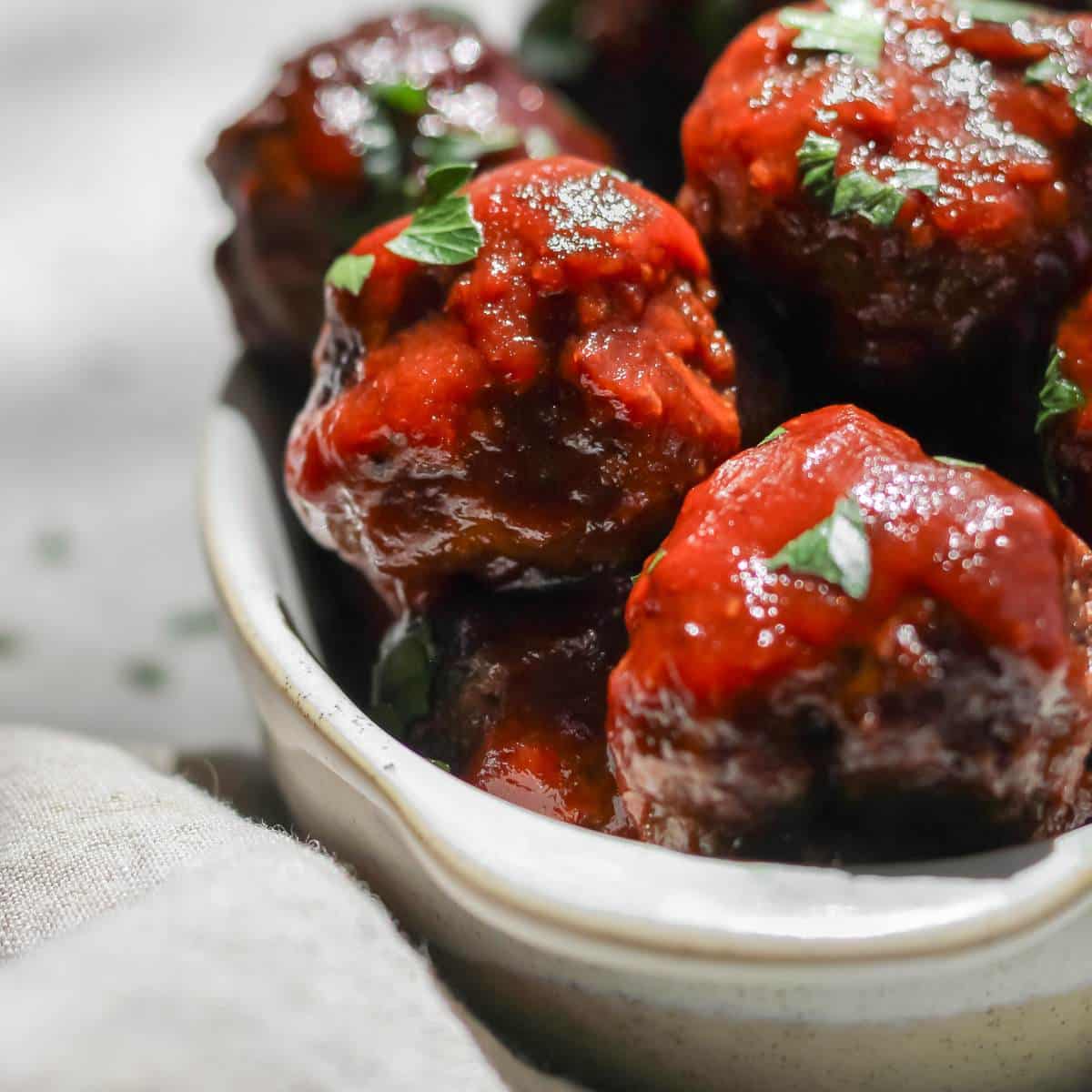 BBQ bison meatballs sprinkled with parsley on top sitting in an oval shaped dish.