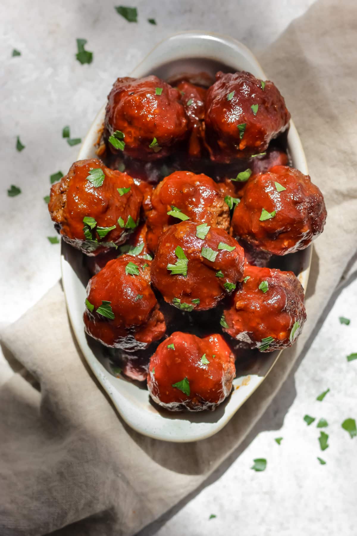 BBQ bison meatballs sprinkled with parsley on top sitting in an oval shaped dish.