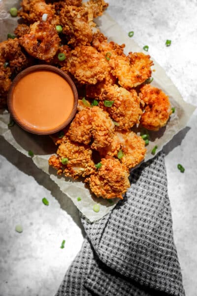 Air fryer panko shrimp on a tray with a side of creamy sriracha sauce in a small ramekin.