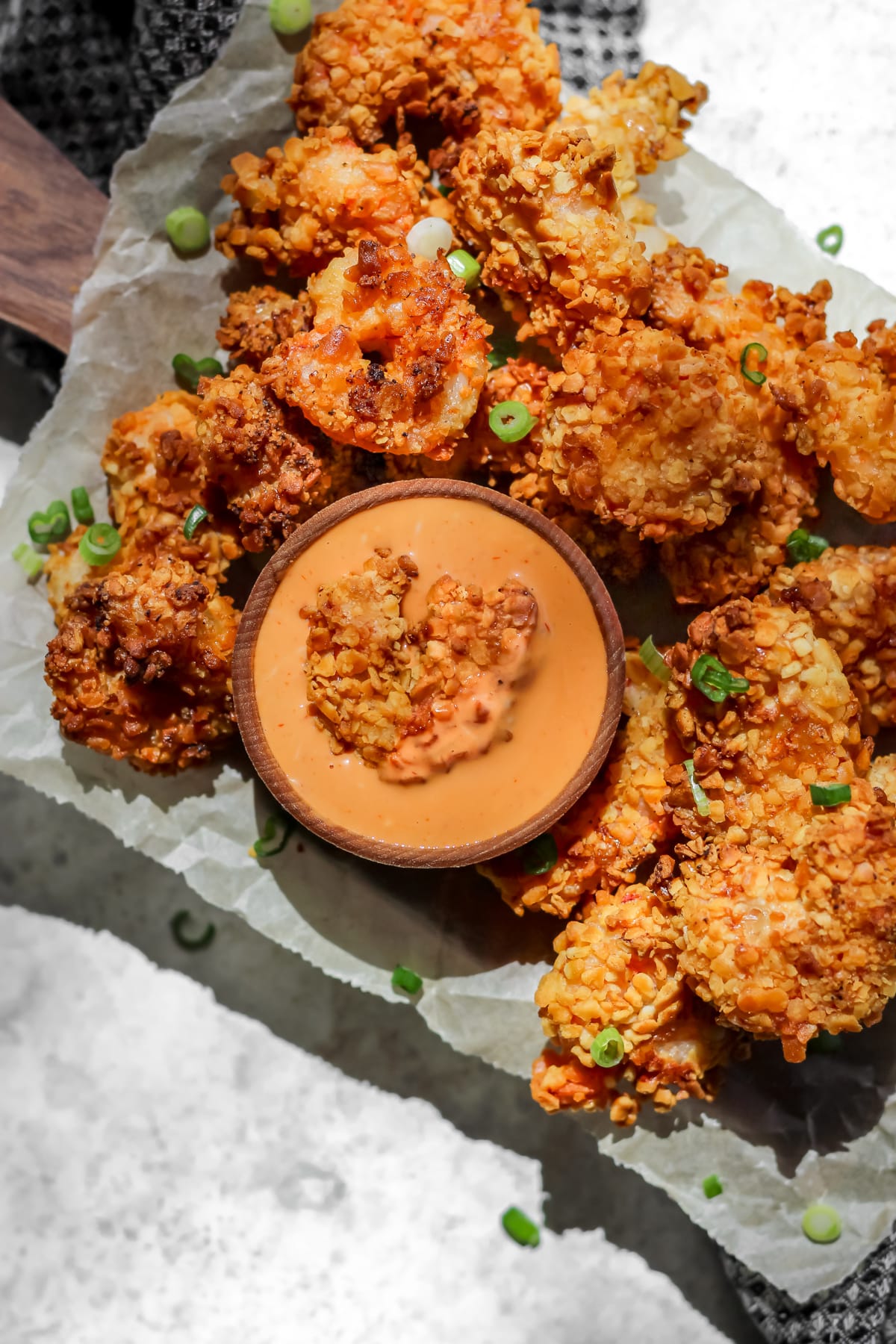 Air fryer panko shrimp on a tray with a side of creamy sriracha sauce in a small ramekin with a panko shrimp inside the sauce.