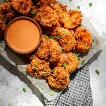 Air fryer panko shrimp on a tray with a side of creamy sriracha sauce in a small ramekin.