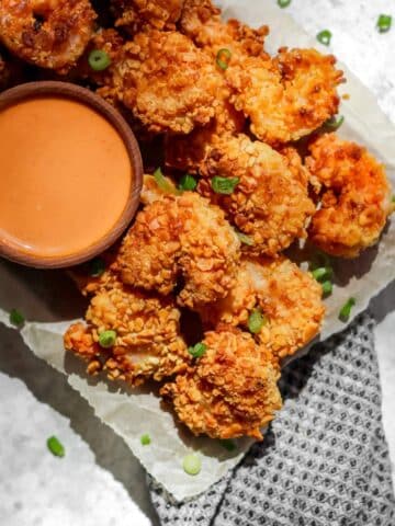 Air fryer panko shrimp on a tray with a side of creamy sriracha sauce in a small ramekin.