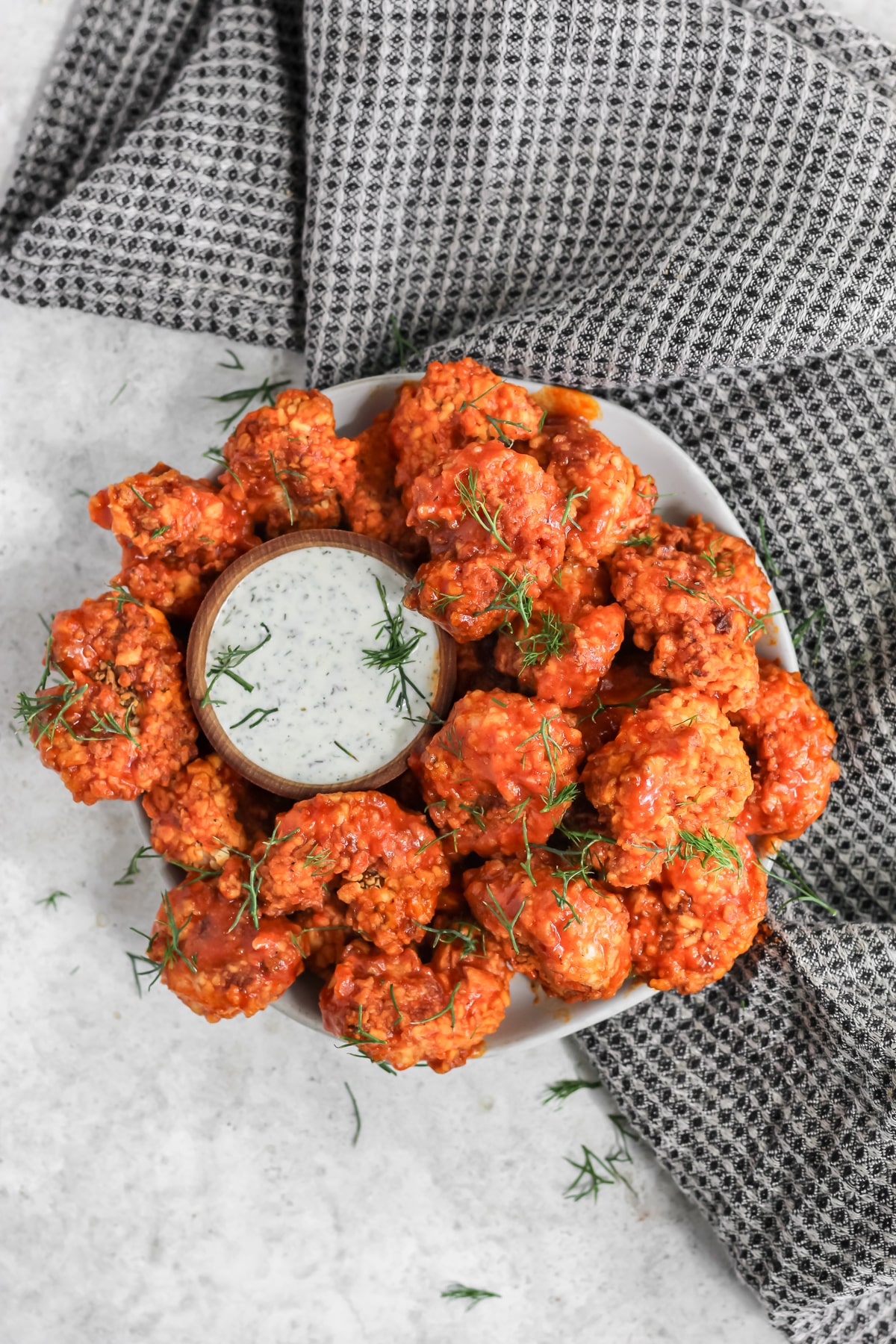 Crispy buffalo shrimp on a plate with a side of ranch and a black and white tea towel next to the plate.