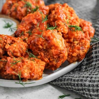 Crispy buffalo shrimp on a plate with a side of ranch and a black and white tea towel next to the plate.